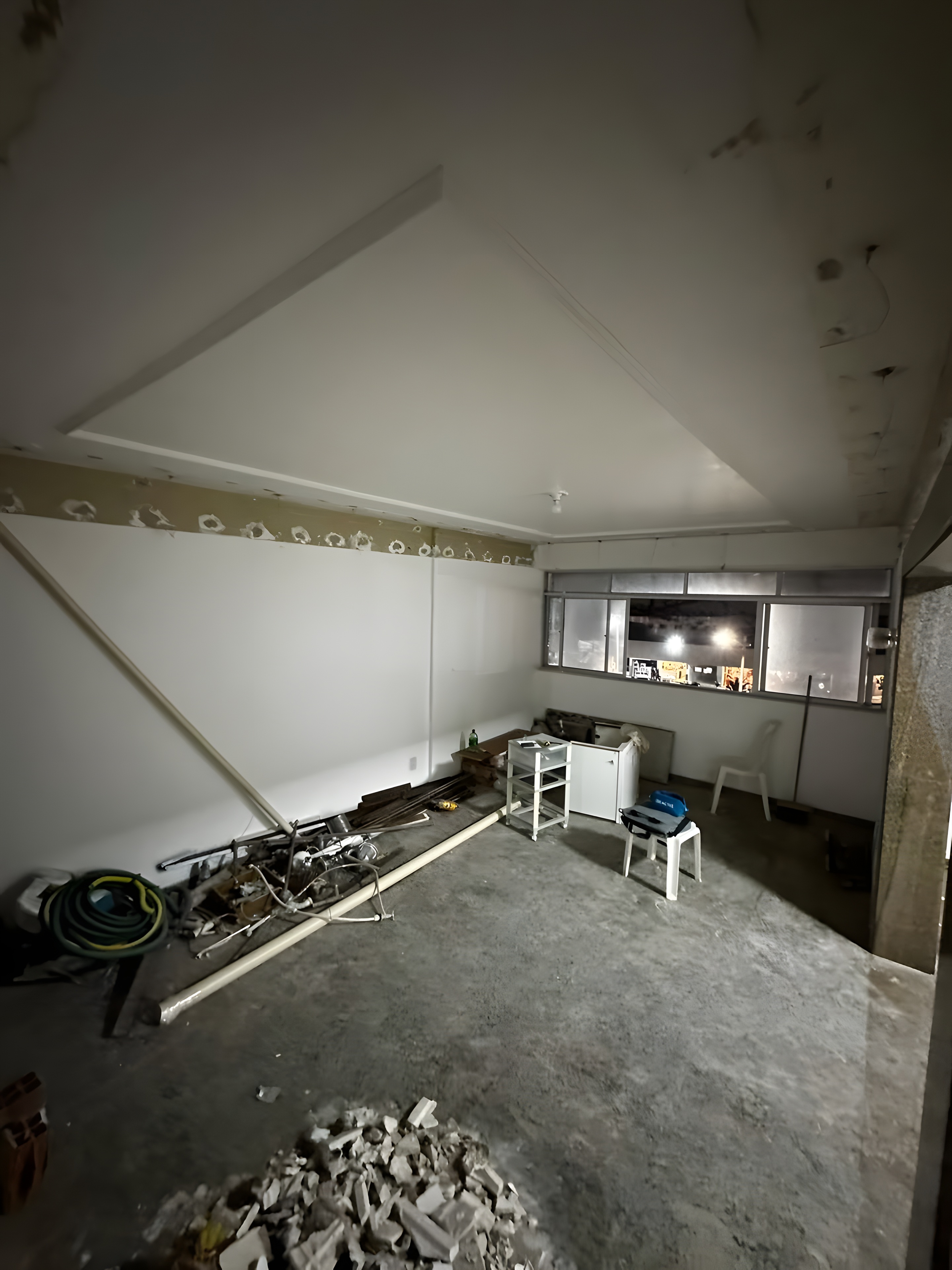 Sala em demolição, com forro rebaixado, janela ao fundo e entulho no piso